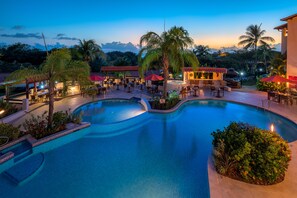 Área de piscina de un complejo turístico con varias zonas de estar y un elemento acuático central.