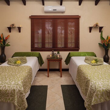 A room with two beds, a small table, and wall-mounted shelves.