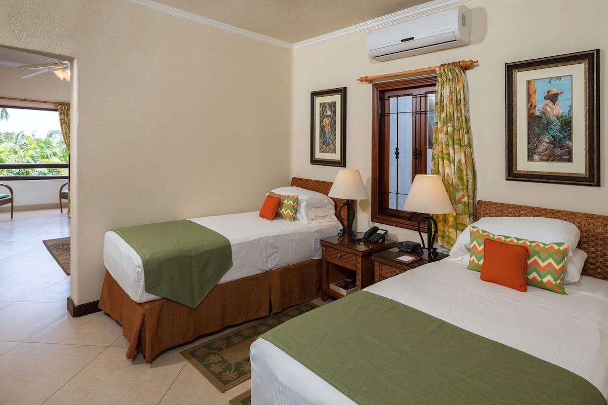 Une chambre d’hôtel avec deux lits, une petite table avec un téléphone, une fenêtre avec des rideaux et un tableau au mur.
