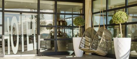 A modern building entrance with large glass doors, a hanging swing chair, and a potted tree.