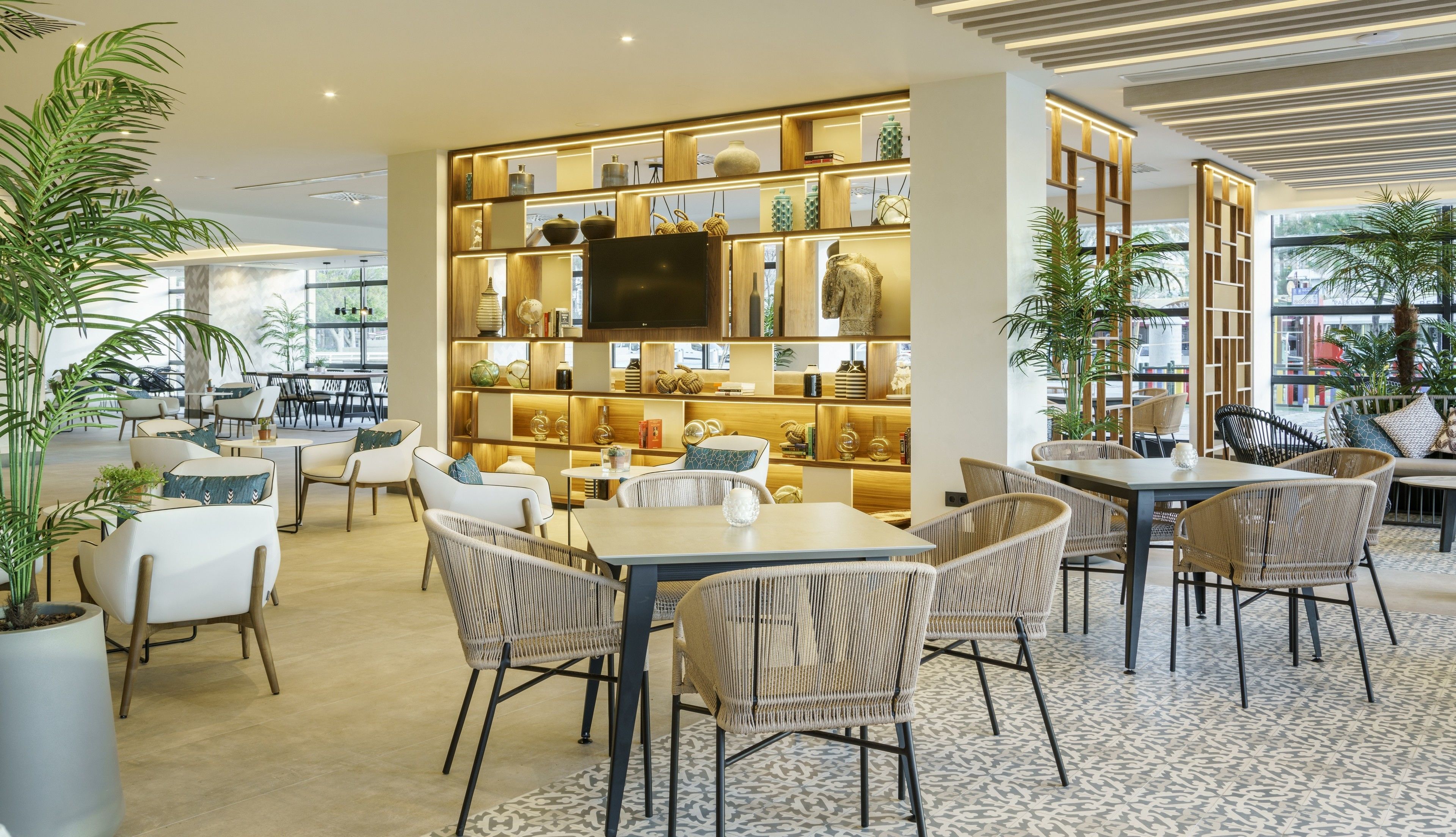 A modern interior with a central seating area, a wooden bookshelf with decorative items, and a large window providing natural light.