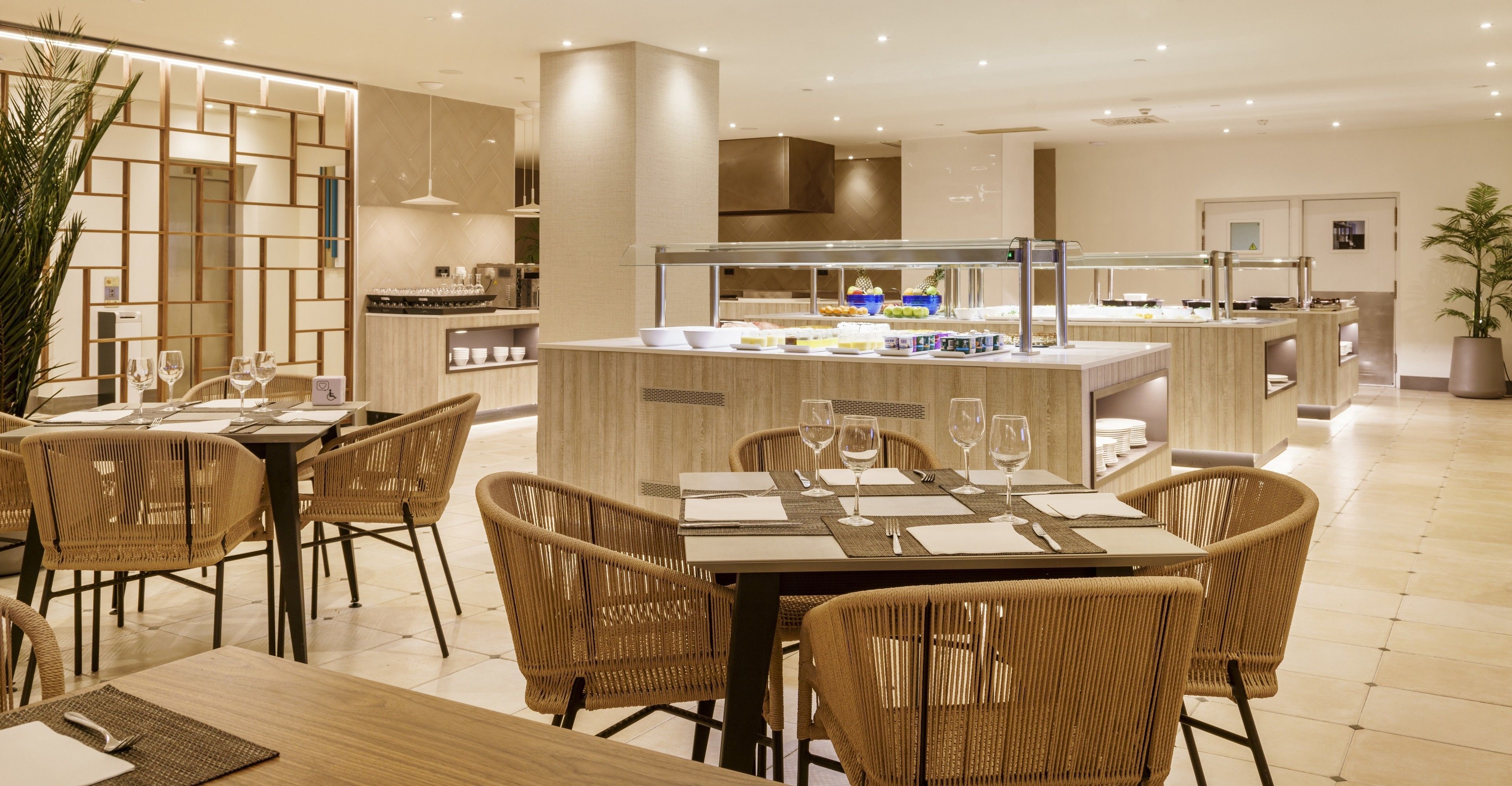 A modern hotel dining area with wicker chairs, a buffet counter, and a clean, well-lit interior.
