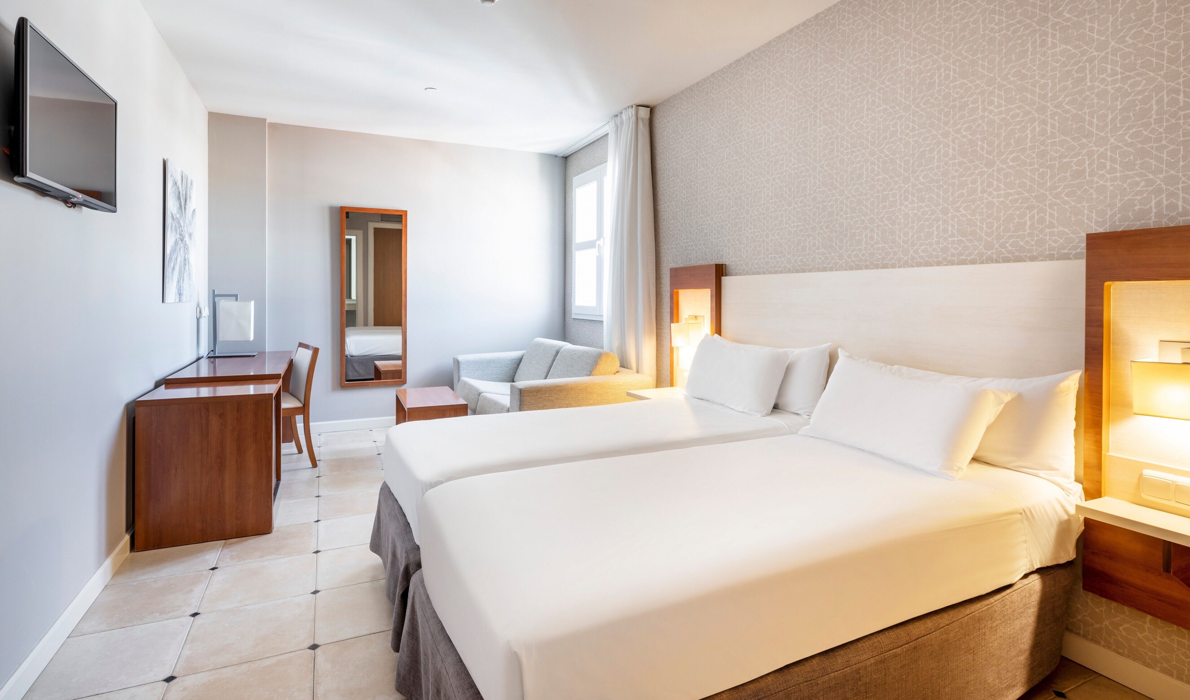 A hotel room with two beds, a desk, a chair, a TV, and a large mirror.