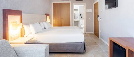 Ein Hotelzimmer mit einem großen Bett, Nachttischen inklusive Lampen, einem an der Wand befestigten Fernseher und einem kleinen Schreibtisch mit Computer.