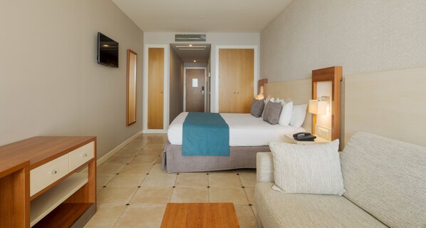 Une chambre d’hôtel équipée d’un lit, d’un bureau, d’un canapé et d’un téléviseur fixé au mur.