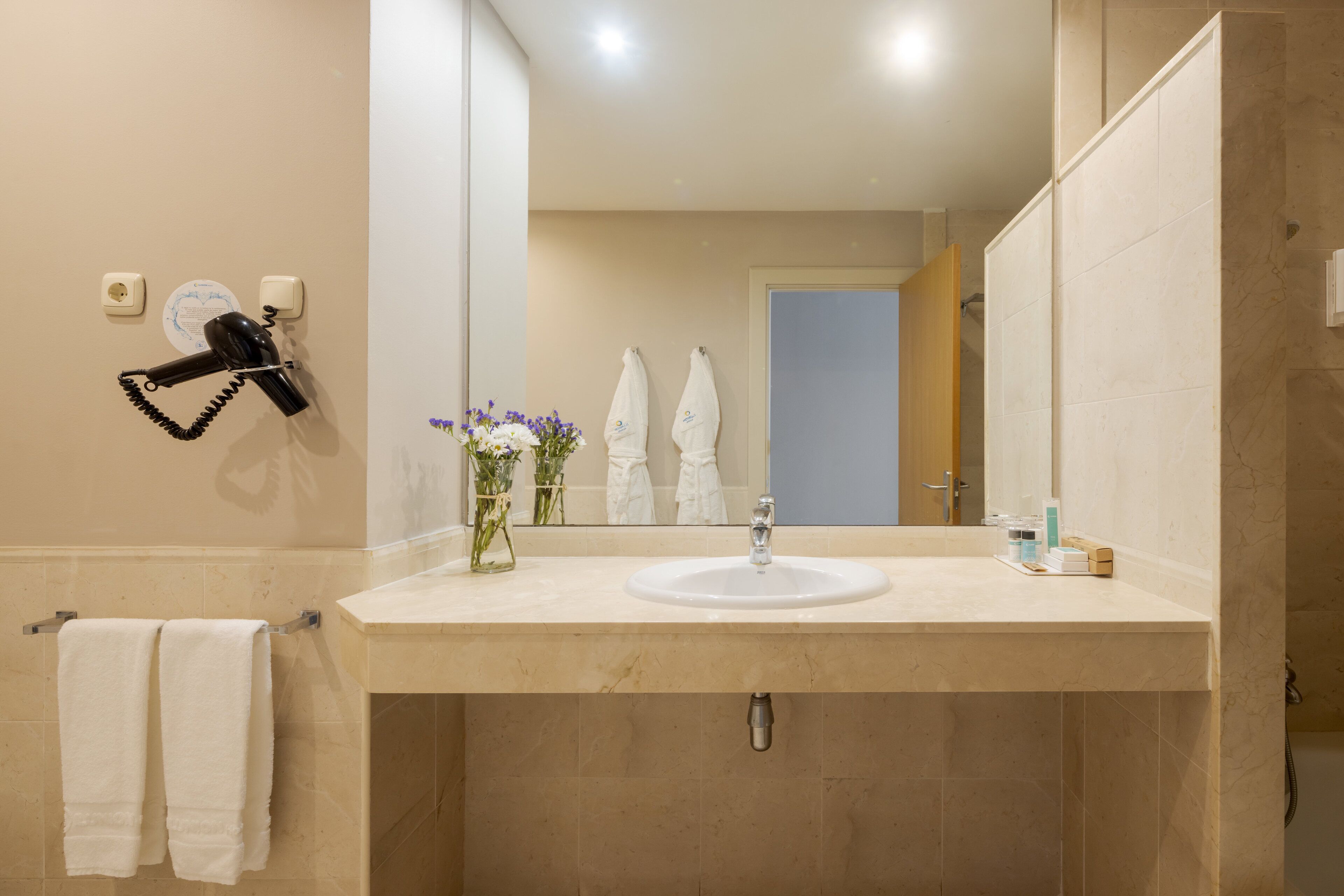 A bathroom with a beige sink, a mirror, a hairdryer, and two towels hanging on hooks.