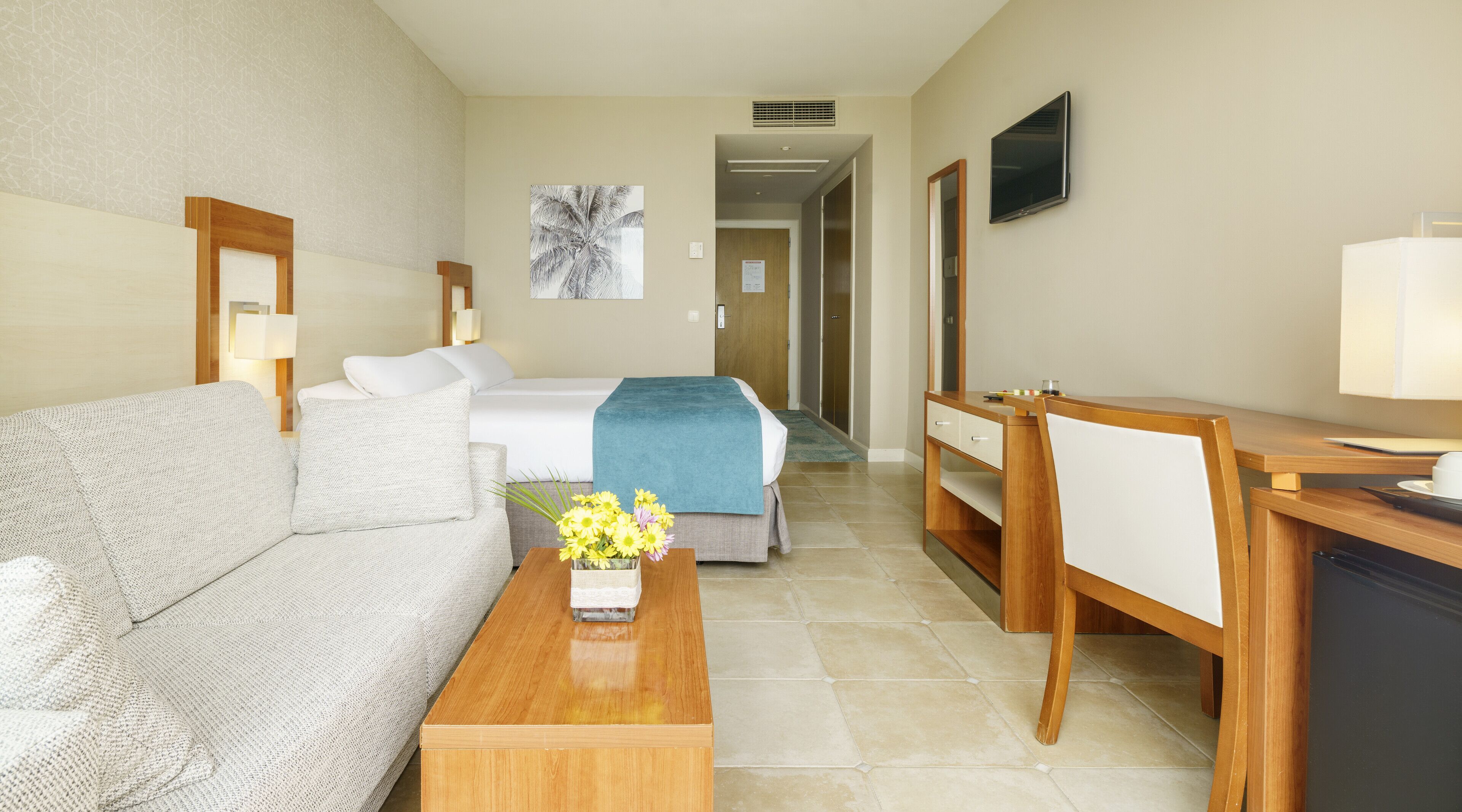 A hotel room with a bed, a sofa, a desk, and a TV.