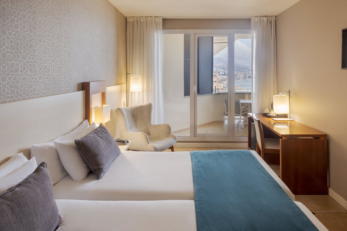 A hotel room with a bed, a desk, a chair, and a balcony with a view.