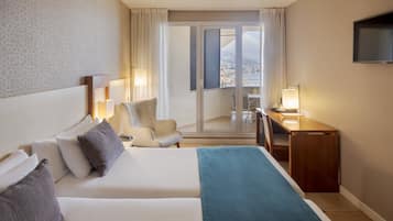 A hotel room with a bed, a desk, a chair, and a balcony with a view.