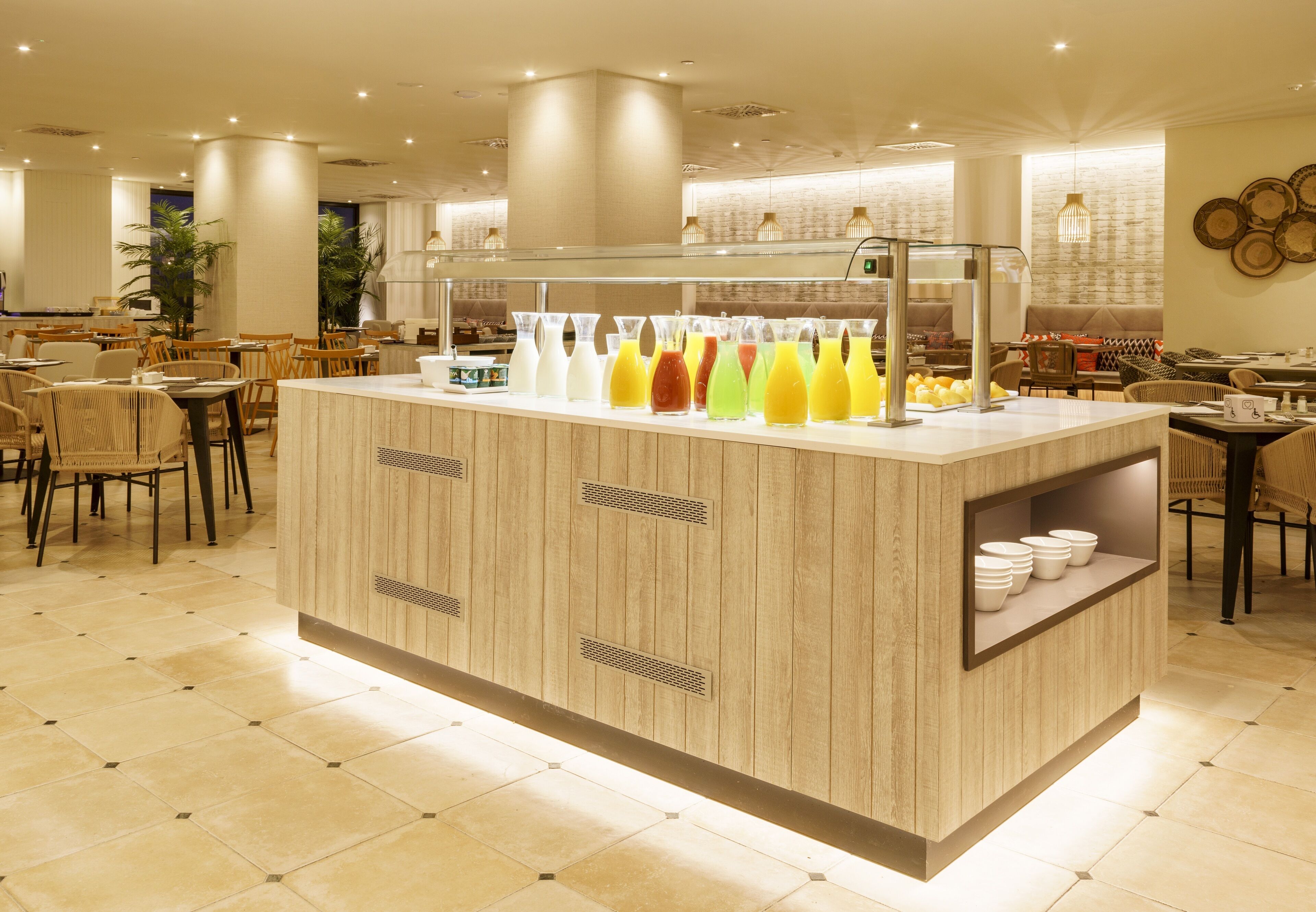 A modern hotel lobby with a central island featuring a juice bar, seating areas, and a buffet line.