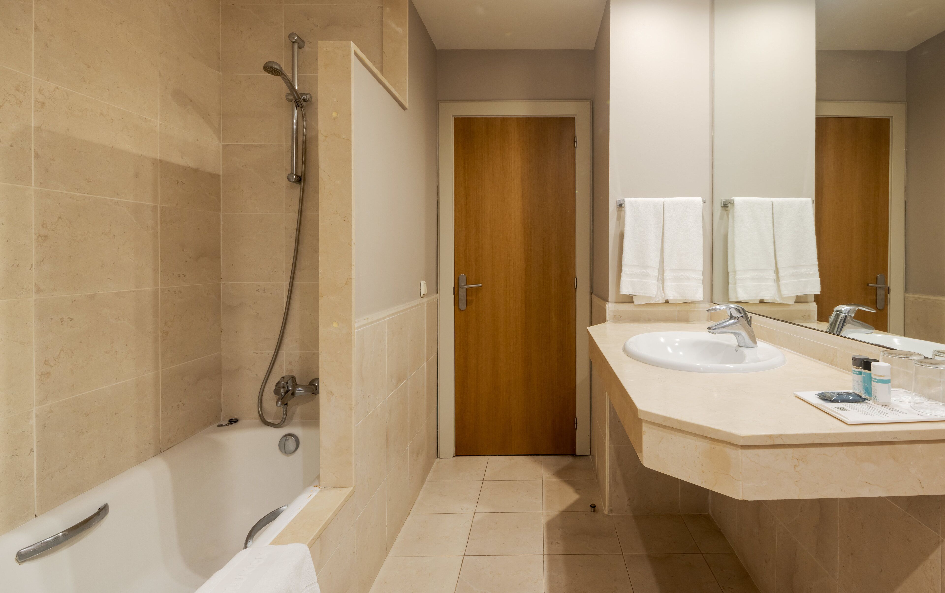 A bathroom with a bathtub, a shower, a sink, and a wooden door.