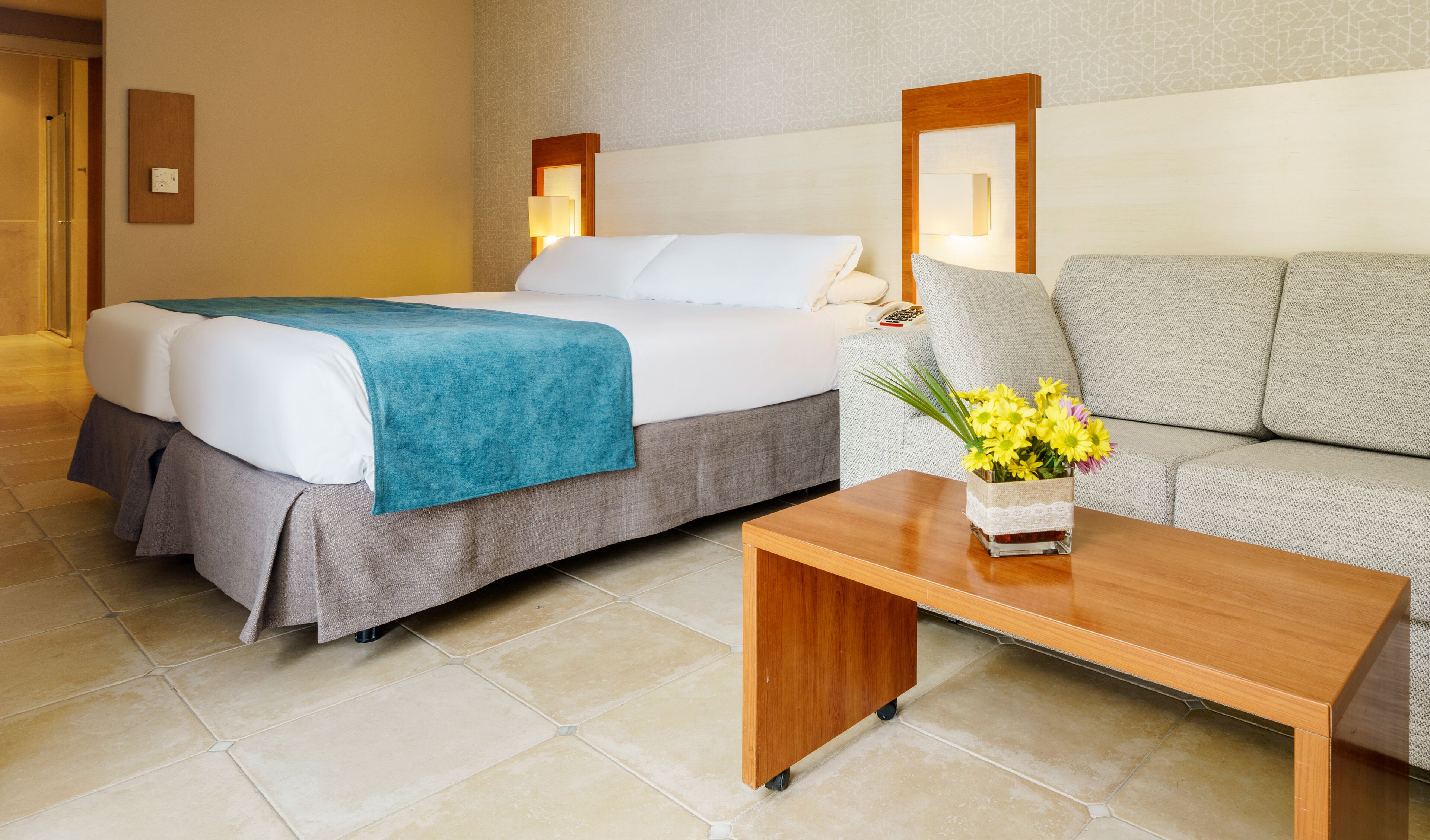 Une chambre d’hôtel avec un lit, un canapé, une table basse et un vase de fleurs.