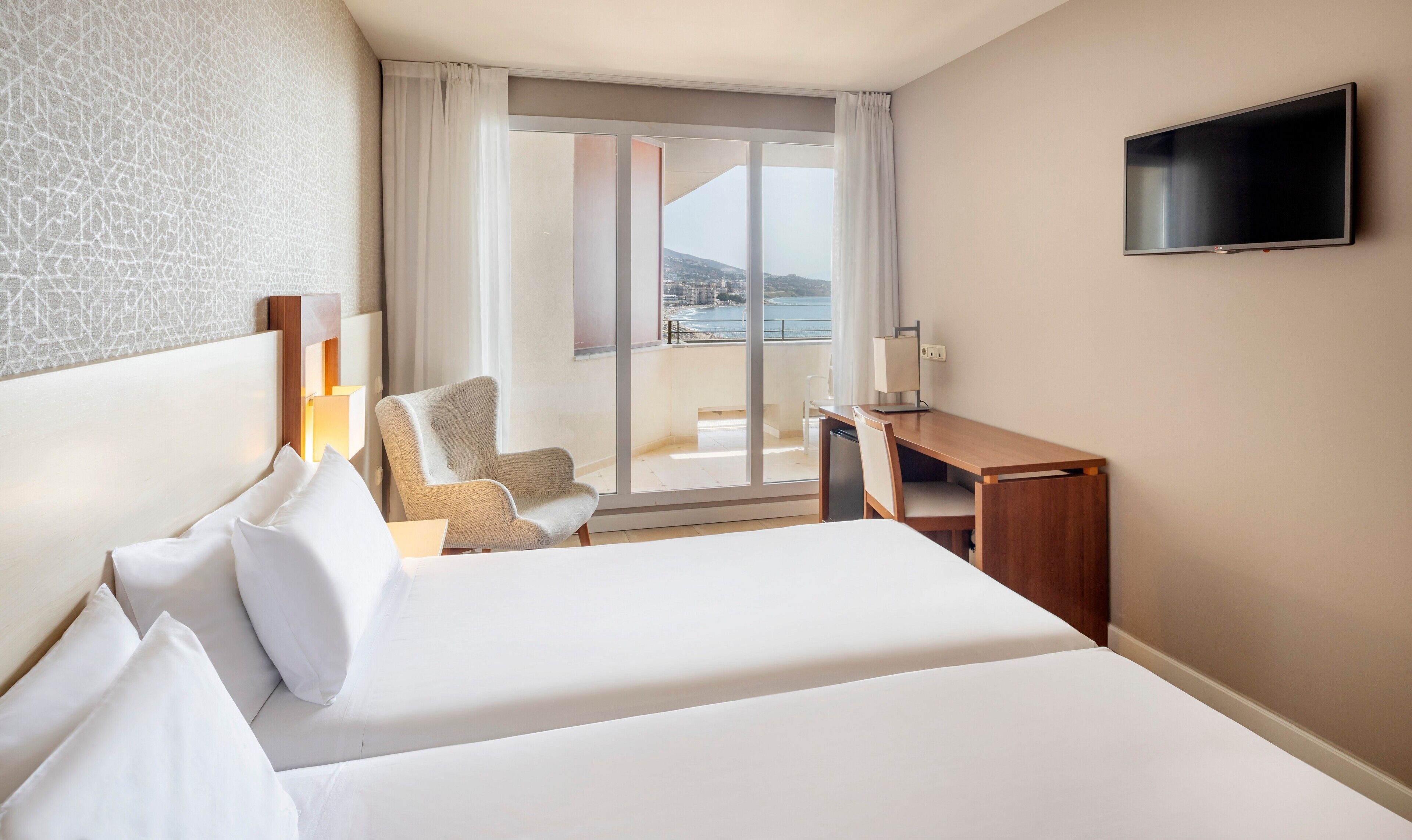 A hotel room with a large bed, a desk, a chair, and a TV.