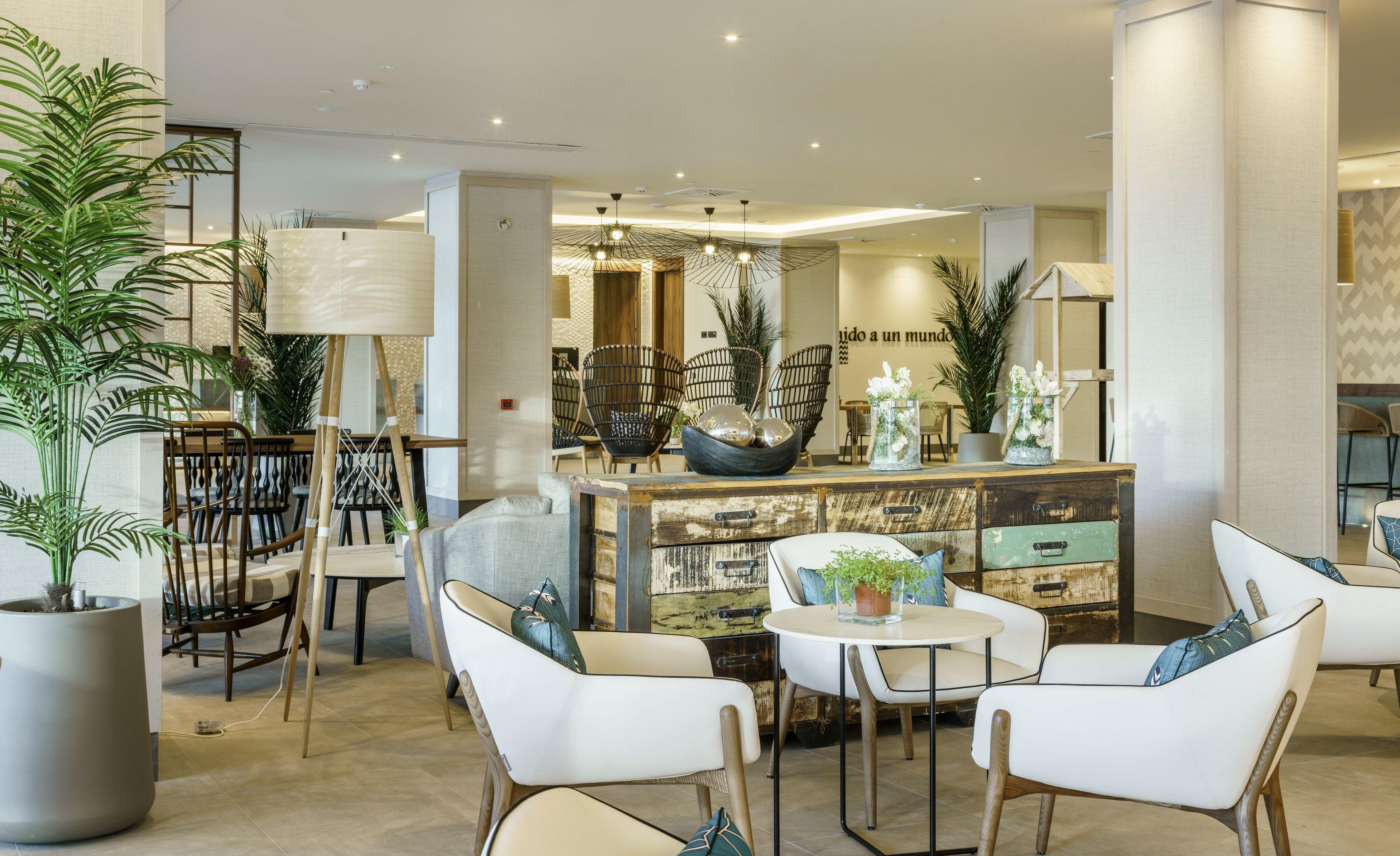 A modern lobby with a central seating area, a decorative wall with a quote, and various plants.