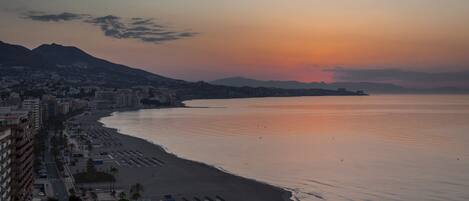 Un paisaje urbano costero con una playa, filas de edificios frente al mar y un cielo despejado.