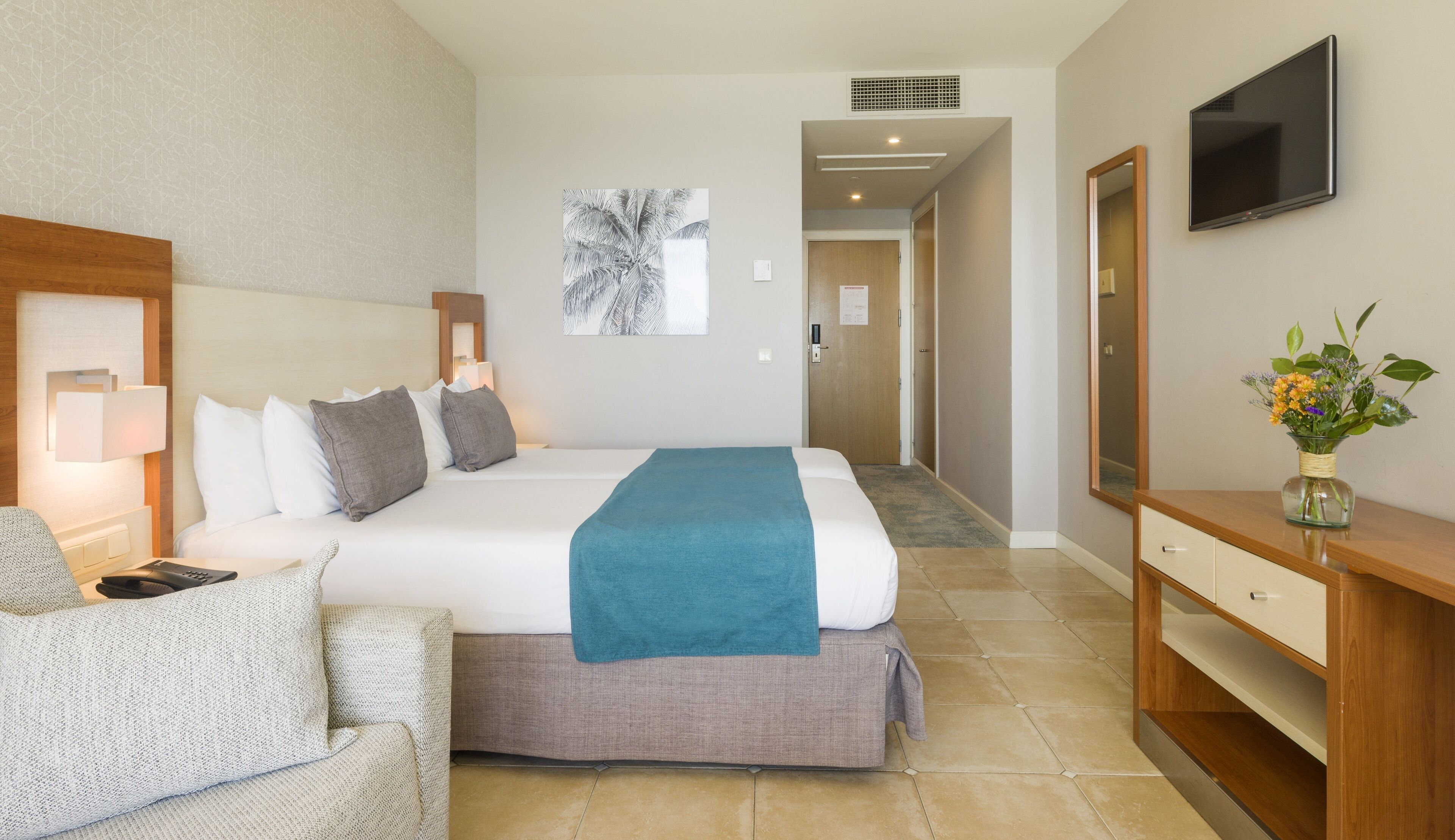 A hotel room with a bed, a desk, a chair, a TV, and a painting on the wall.