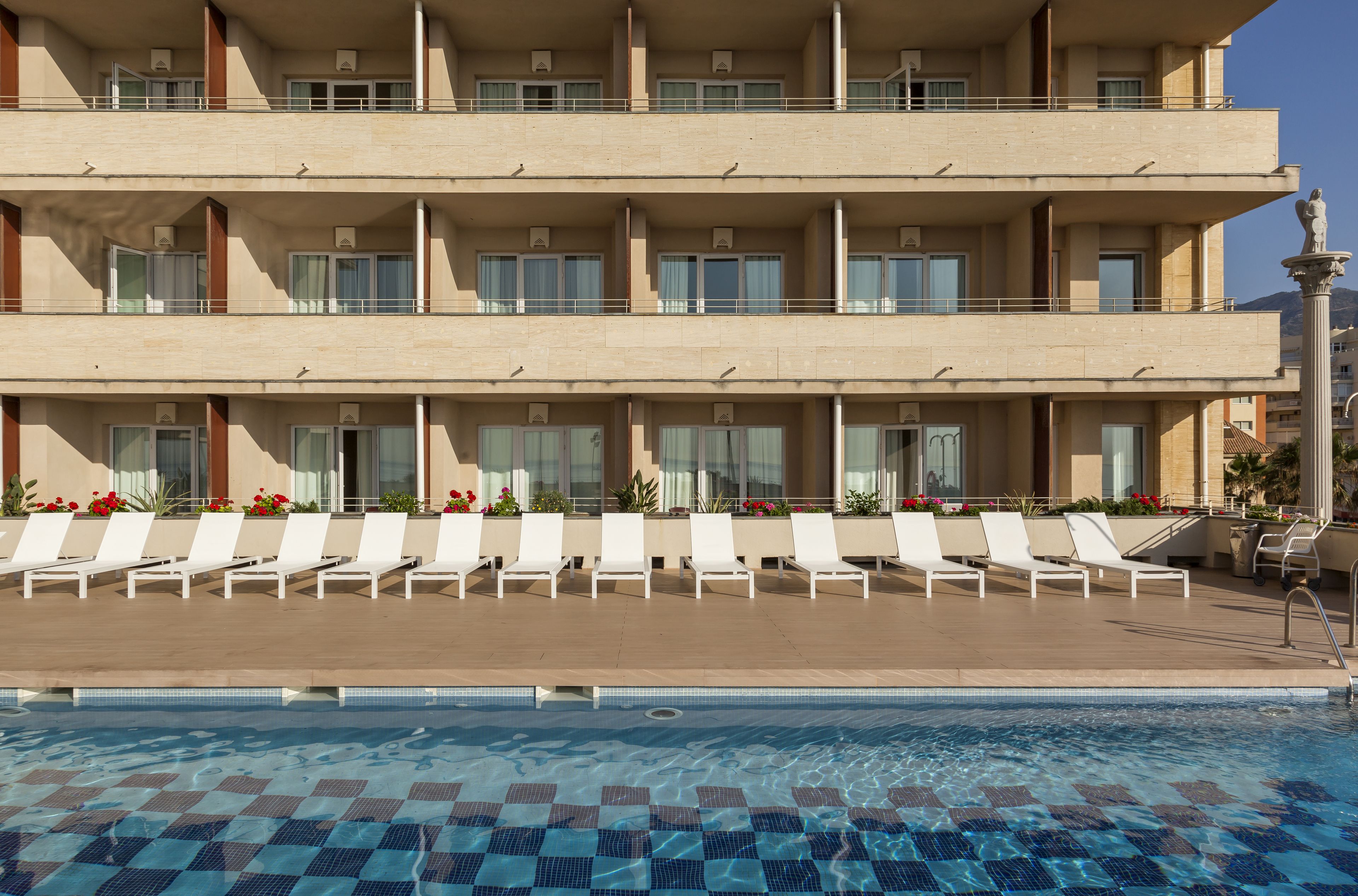 A hotel with a pool area featuring sun loungers and a clear blue pool.
