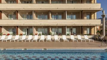 A hotel with a pool area featuring sun loungers and a clear blue pool.