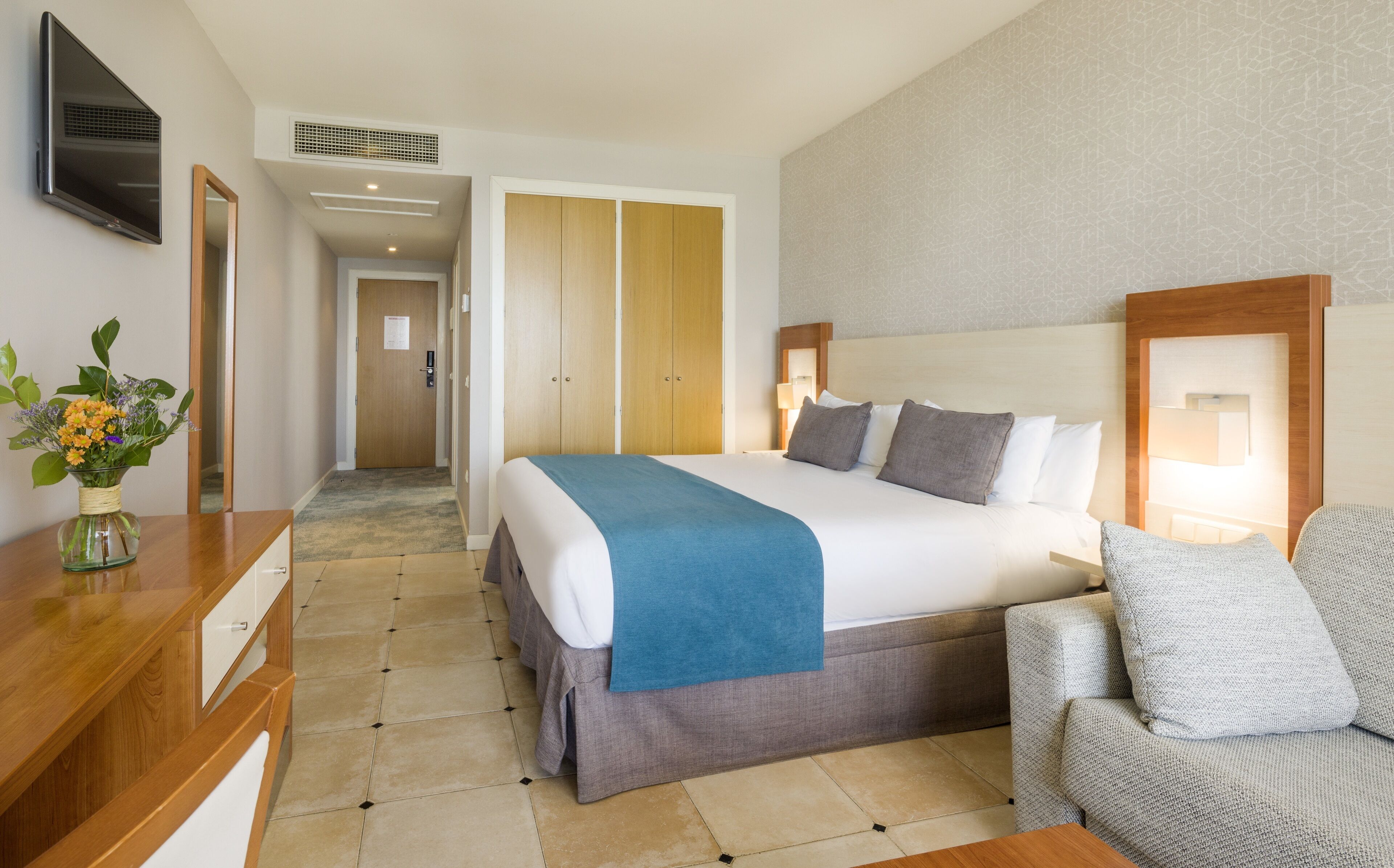 Habitación de hotel con cama, escritorio, silla, televisor y baño con ducha.