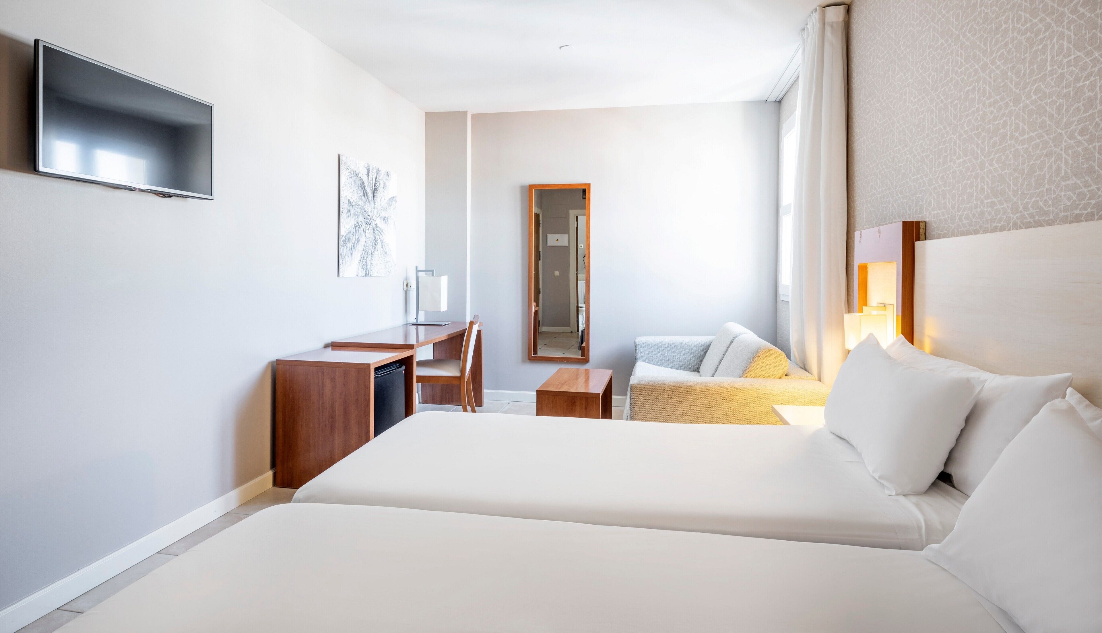 A hotel room with a large bed, a desk, a chair, a mirror, and a television.