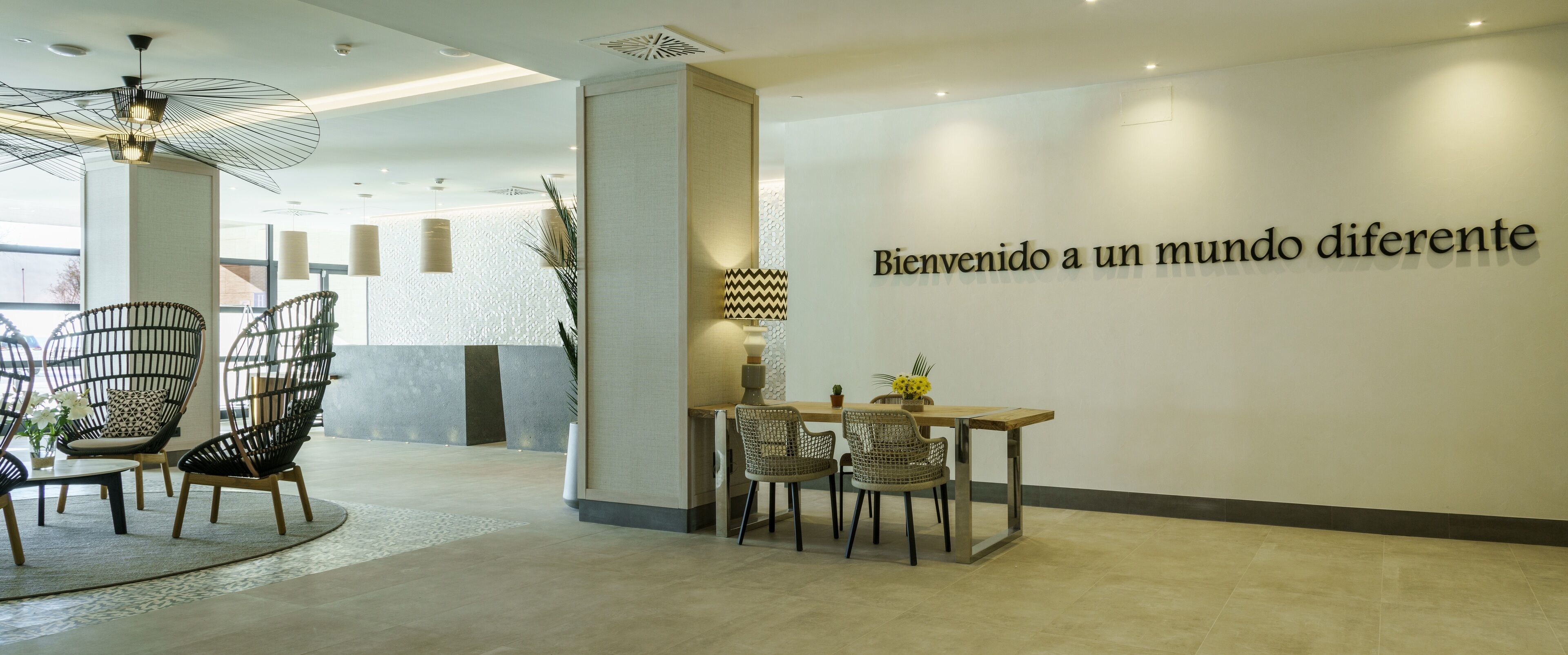A modern reception area with wicker chairs, a wooden table, and a wall with a welcoming message.