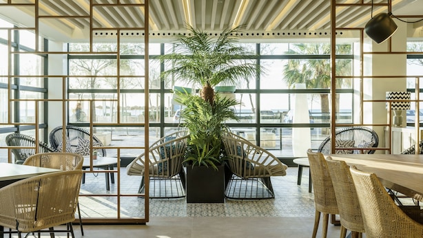 Un interior moderno con ventanas amplias, mobiliario de mimbre y una planta central.