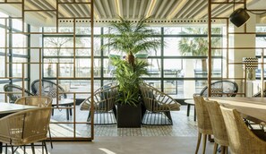 Un interior moderno con ventanas amplias, mobiliario de mimbre y una planta central.