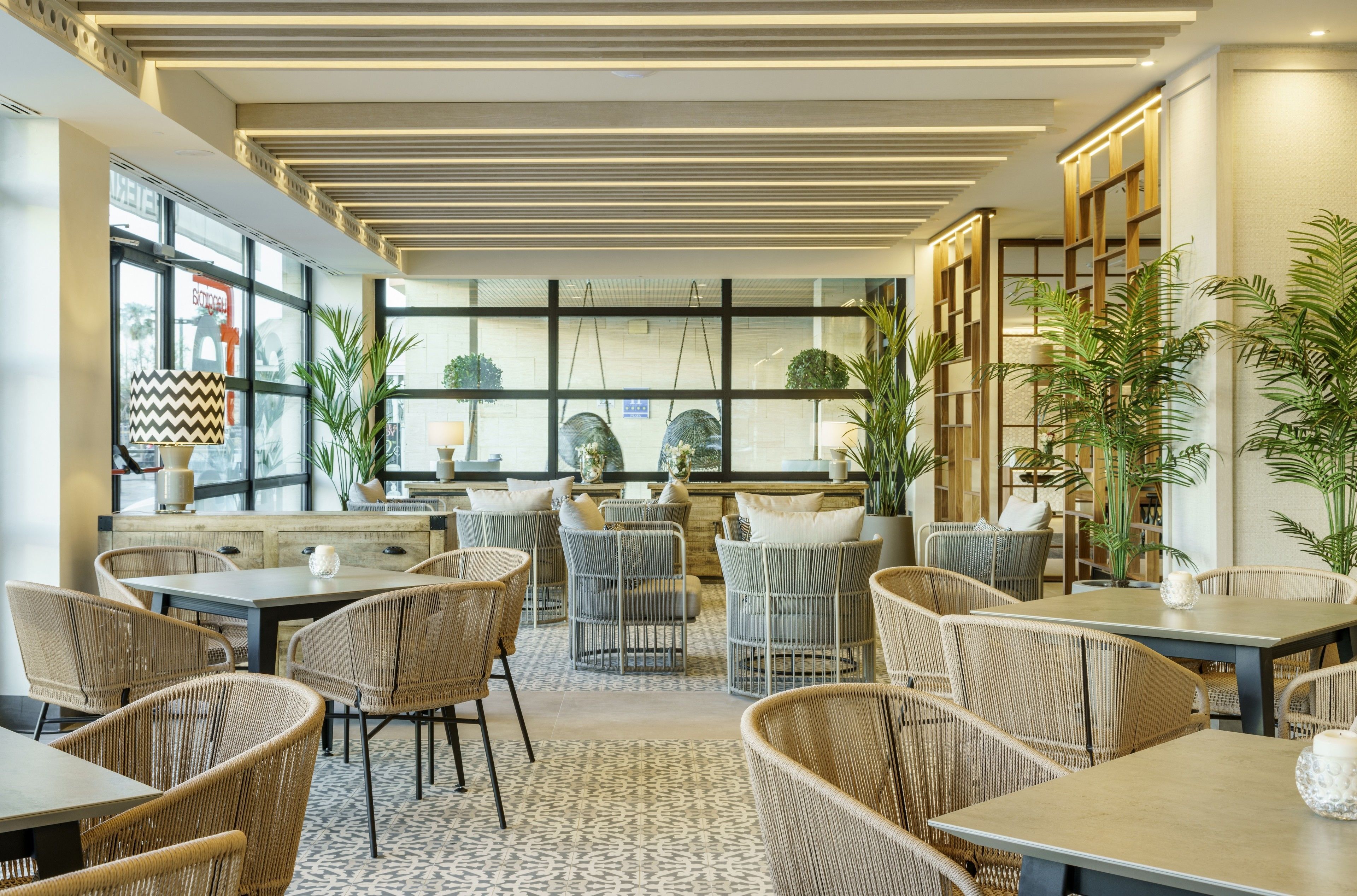 A modern indoor seating area with wicker furniture, large windows, and indoor plants.