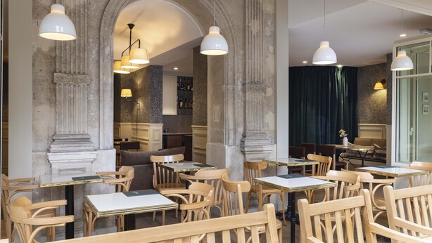Un restaurante con mesas y sillas de madera, columnas de piedra e iluminación colgante.