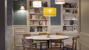 A dining area with a round table, six chairs, and a bowl of fruit. There are two bookshelves with books and decorative items.