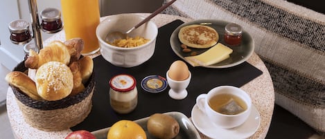 Un plateau de petit-déjeuner avec du pain, des fruits, des céréales, des crêpes, du fromage et du thé.