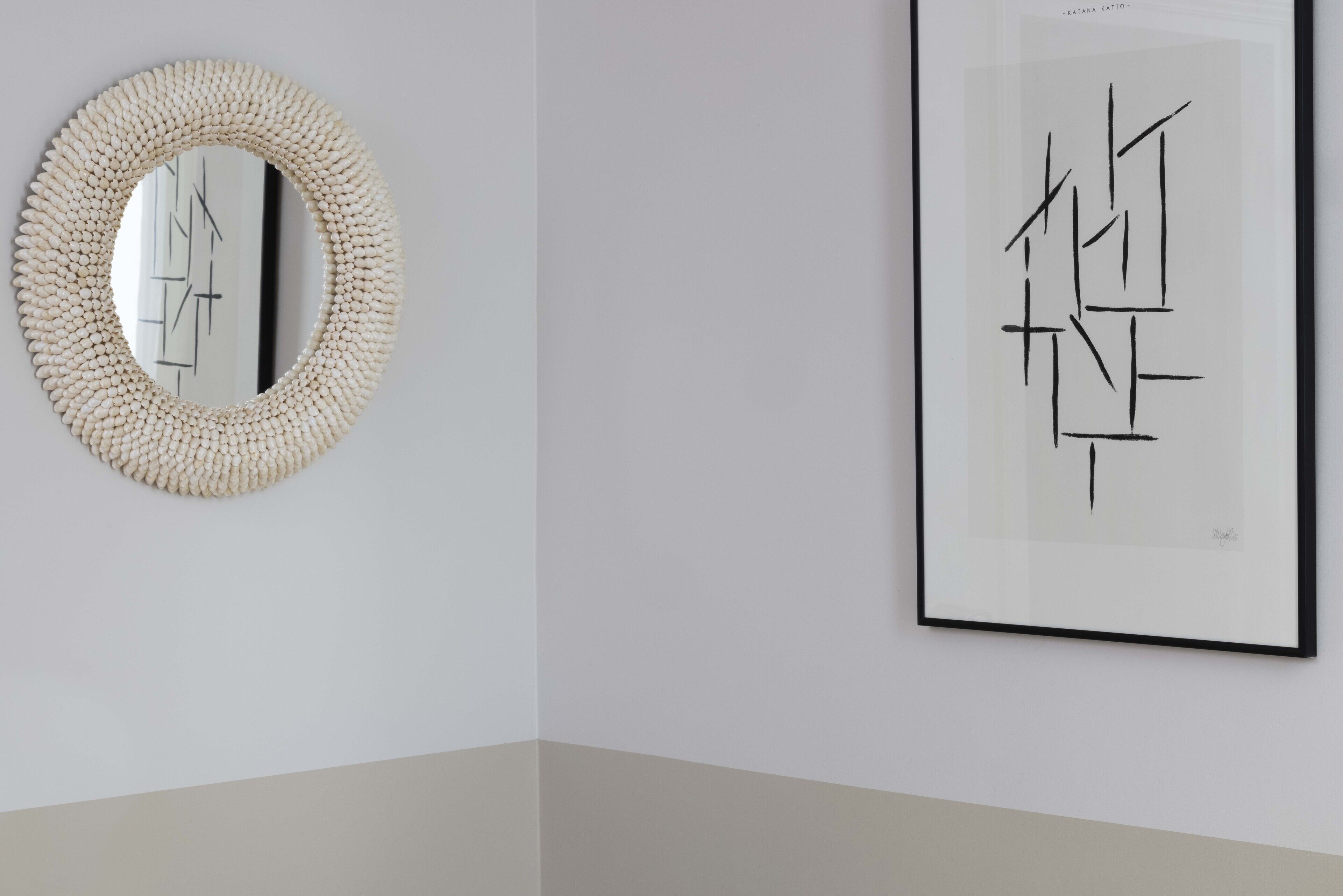 A framed abstract artwork and a textured mirror on a plain wall.