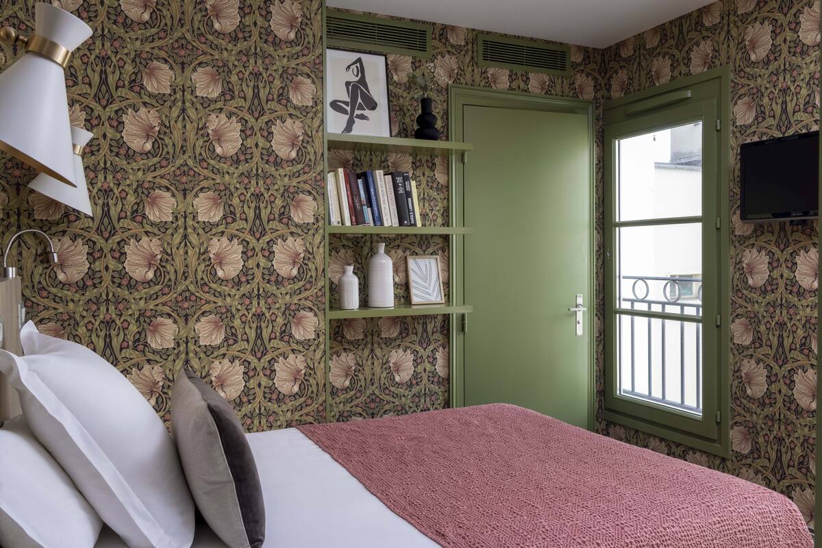 Ein Schlafzimmer mit einem Bett, Kissen, einem Bücherregal, einer grünen Tür und einem Fenster mit Balkon.