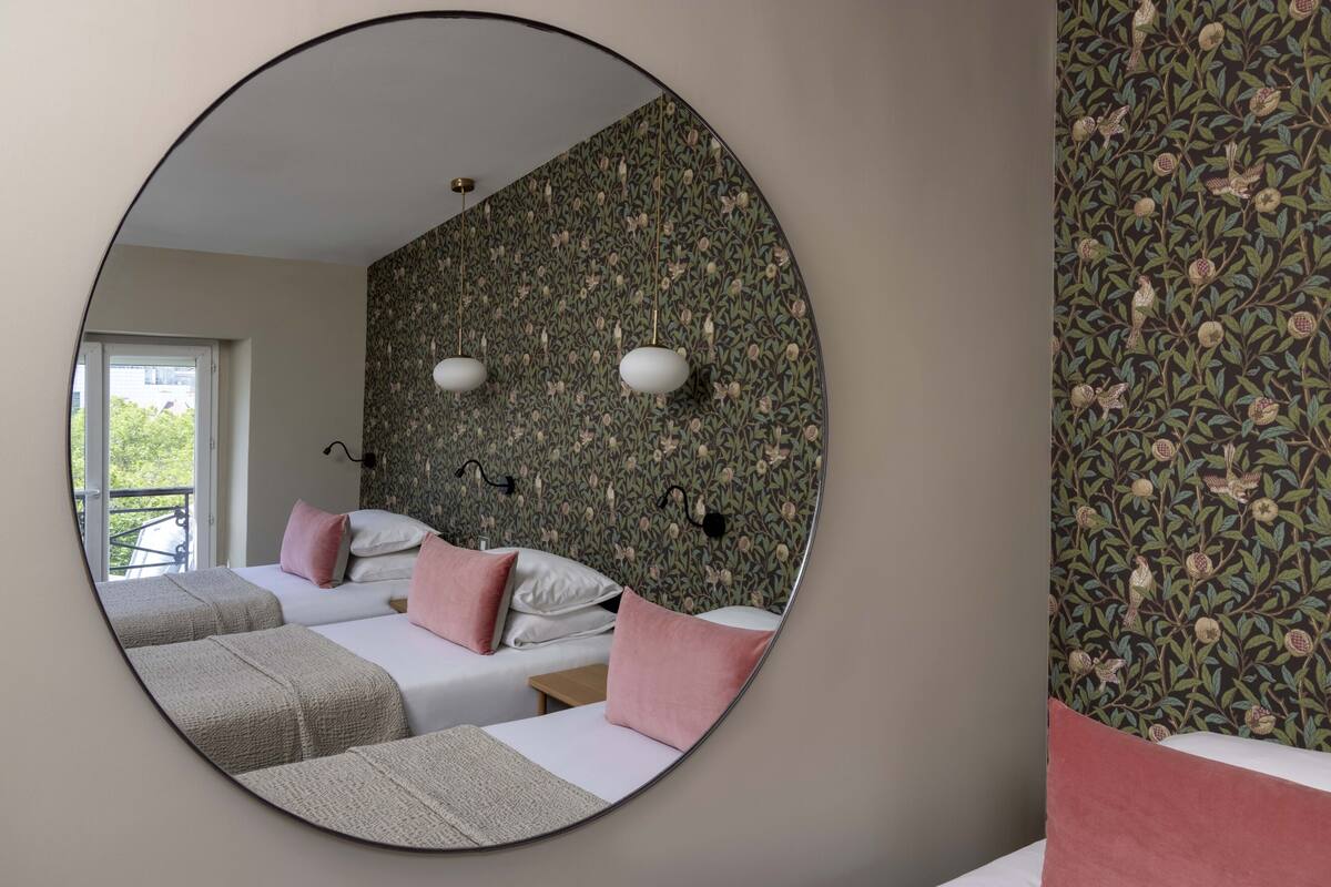 Ein Schlafzimmer mit zwei Betten, einem runden Spiegel und blumigem Wandpapier.