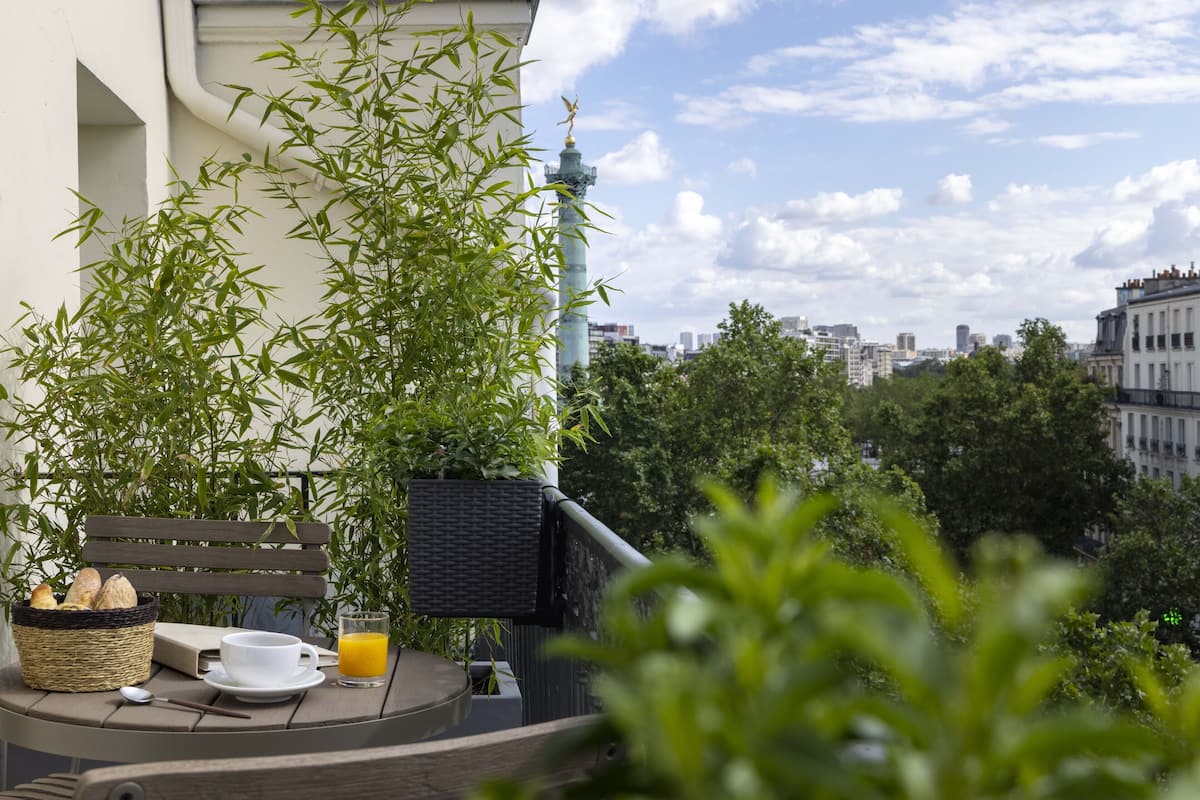 Ein Balkon mit einem Korbstuhl, einem Korb mit Brot, einer weißen Tasse und einem Glas Orangensaft.