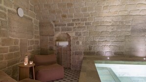 Una habitación con paredes de piedra, una pequeña mesa redonda, un banco acolchado y una bañera con cubierta de vidrio.