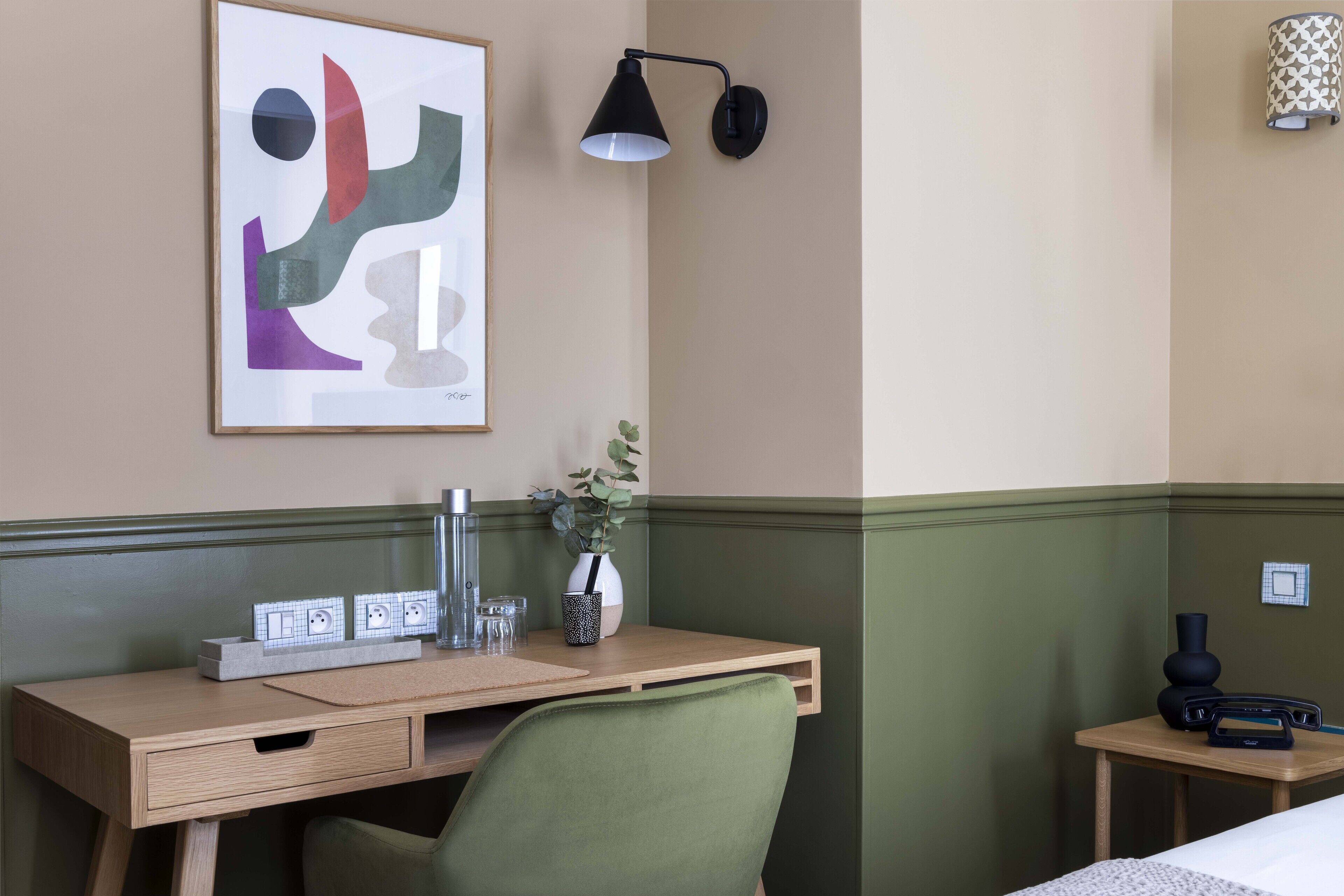 Une chambre d’hôtel équipée d’un bureau, d’une chaise, d’œuvres d’art, d’une lampe, d’un vase et d’un lit.