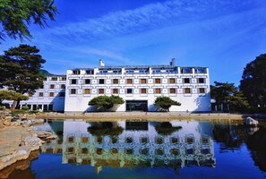 A large white building with multiple balconies and a reflection in the water. - BTG Fragrant Hill Hotel (Beijing)