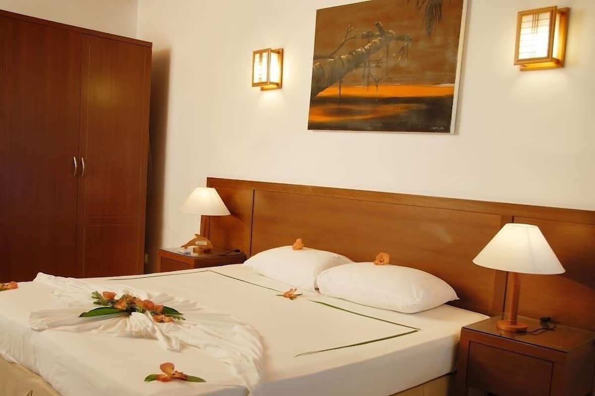 A hotel room with a wooden headboard, a large bed with white linens, two bedside lamps, a nightstand, and a painting on the wall.