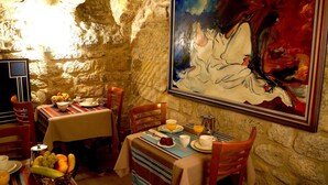 A dining area with stone walls, a table set with plates, glasses, and a fruit basket. - Hôtel Danemark (Paris)
