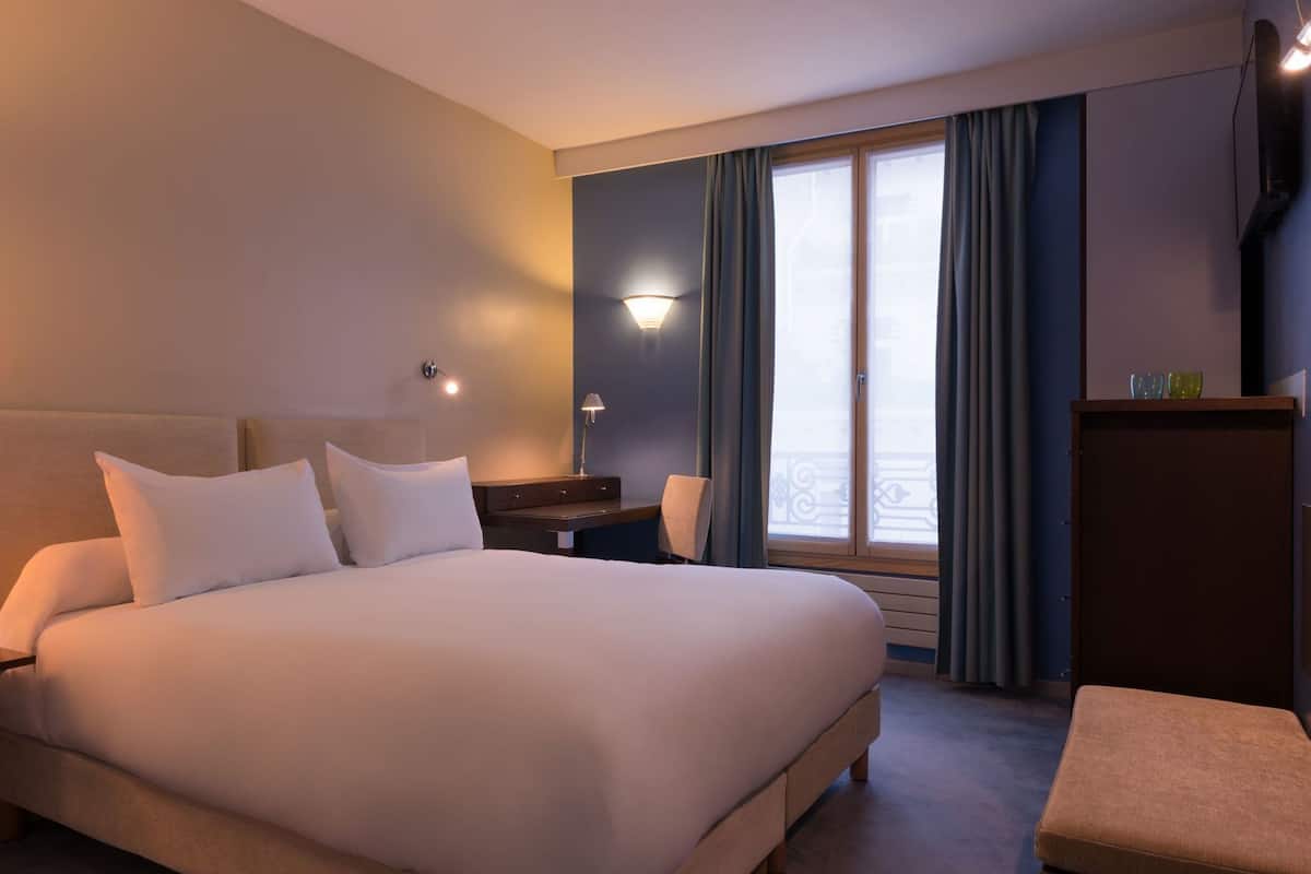 A hotel room with a large bed, bedside tables, a desk, and a window with curtains.