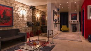 A modern living room with a stone wall, a sofa, a glass coffee table, and a yellow armchair. - Hôtel Danemark (Paris)