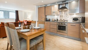 A modern kitchen with wooden cabinets, stainless steel appliances, and a dining area with a wooden table and chairs. - PREMIER SUITES Newcastle (Newcastle-upon-Tyne)