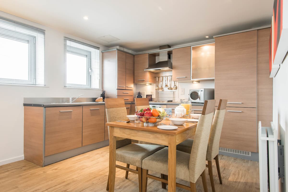 Een moderne keuken met houten kastjes, een eettafel met stoelen en een fruitschaal op de tafel.