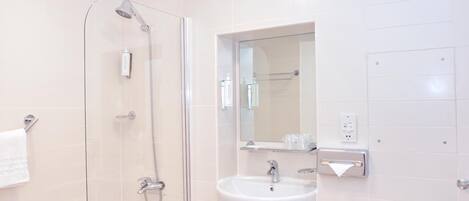 Ein modernes Badezimmer mit einer gläsernen Duschkabine, einem weißen Waschbecken und einem Spiegel darüber.