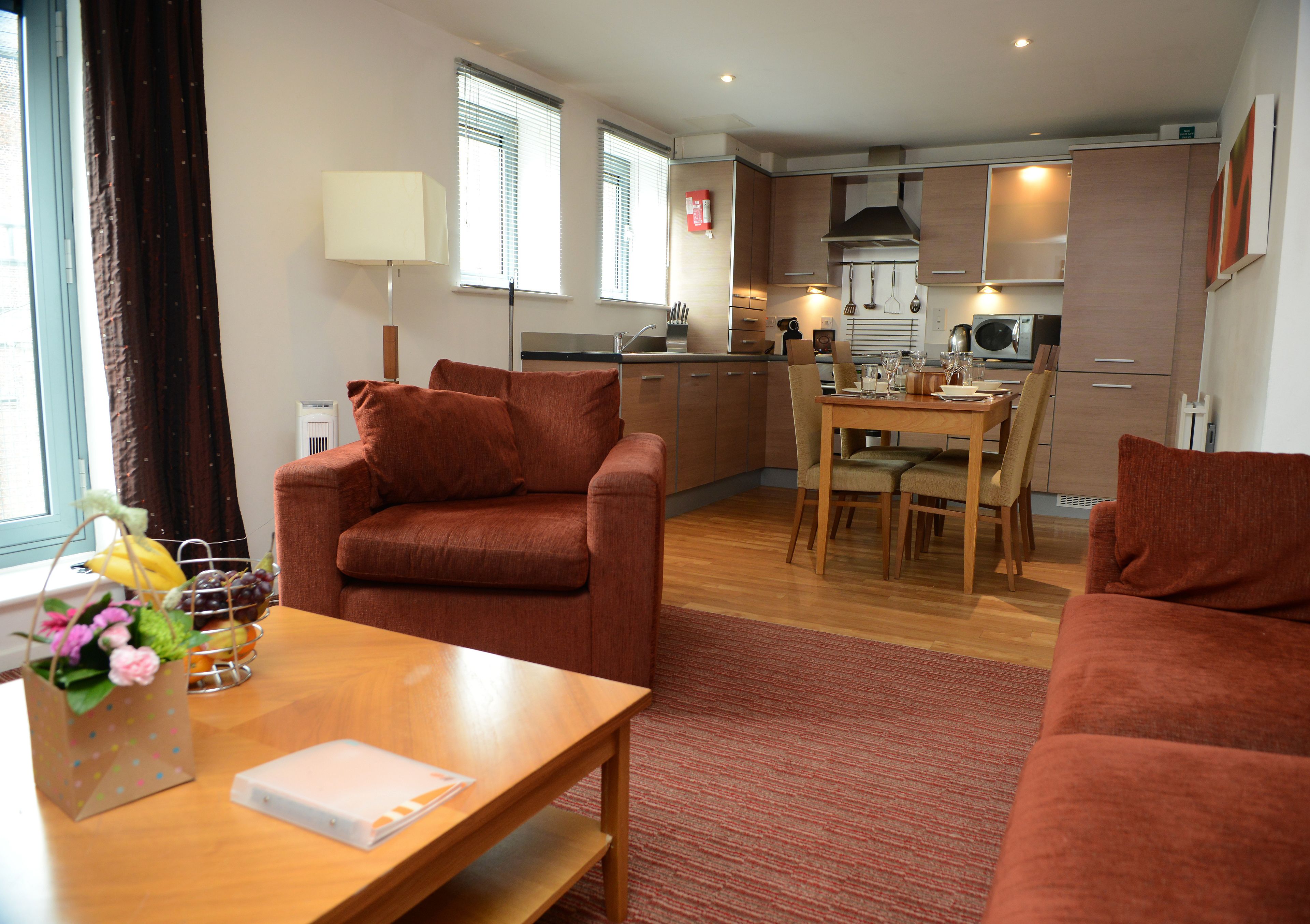 A modern living room with a sofa, a dining table, and a kitchen in the background.