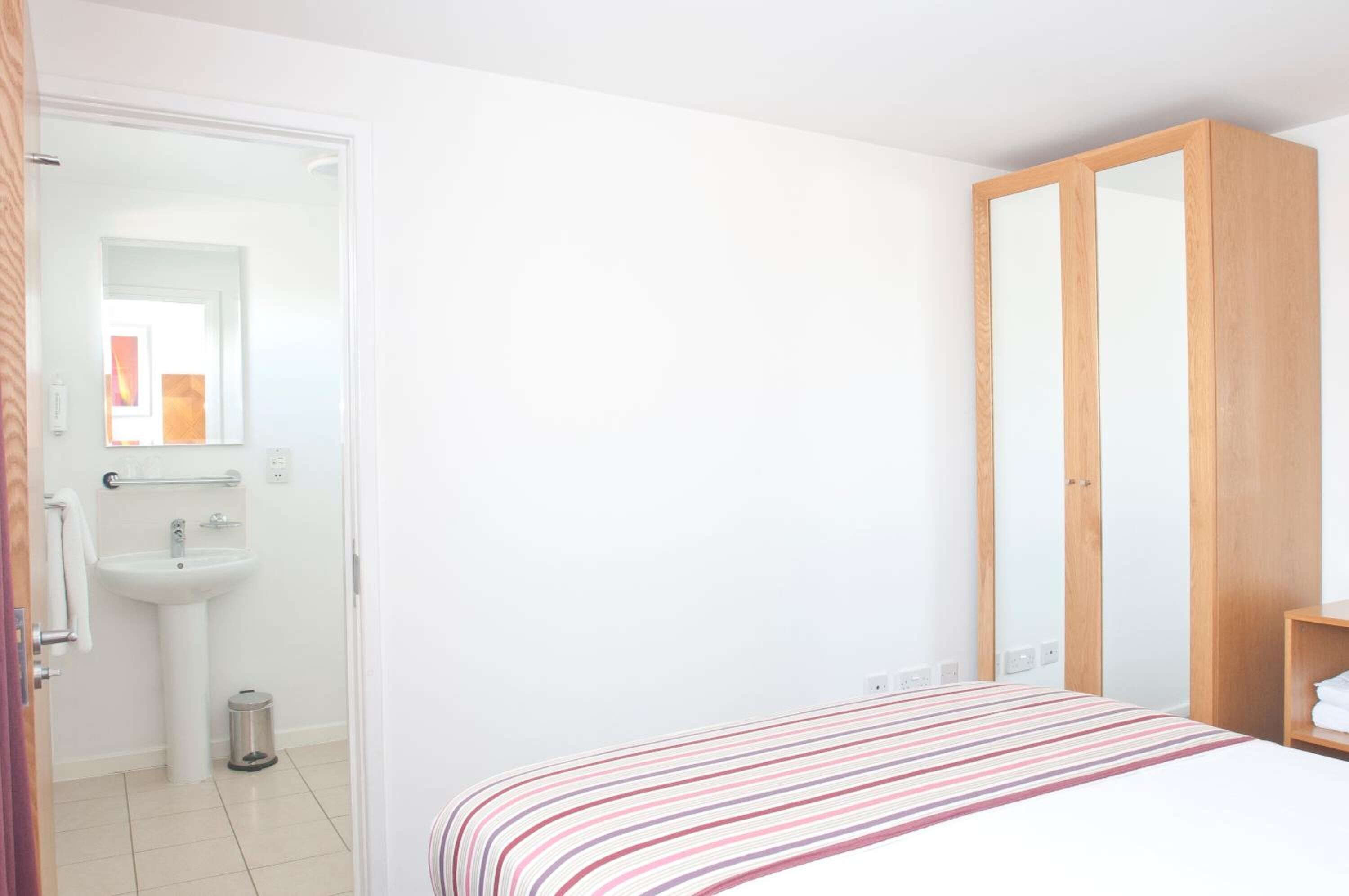 Un dormitorio con cama, armario y baño con lavabo y espejo.