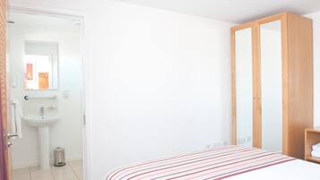 Un dormitorio con cama, armario y baño con lavabo y espejo.