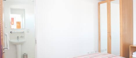 Un dormitorio con cama, armario y baño con lavabo y espejo.
