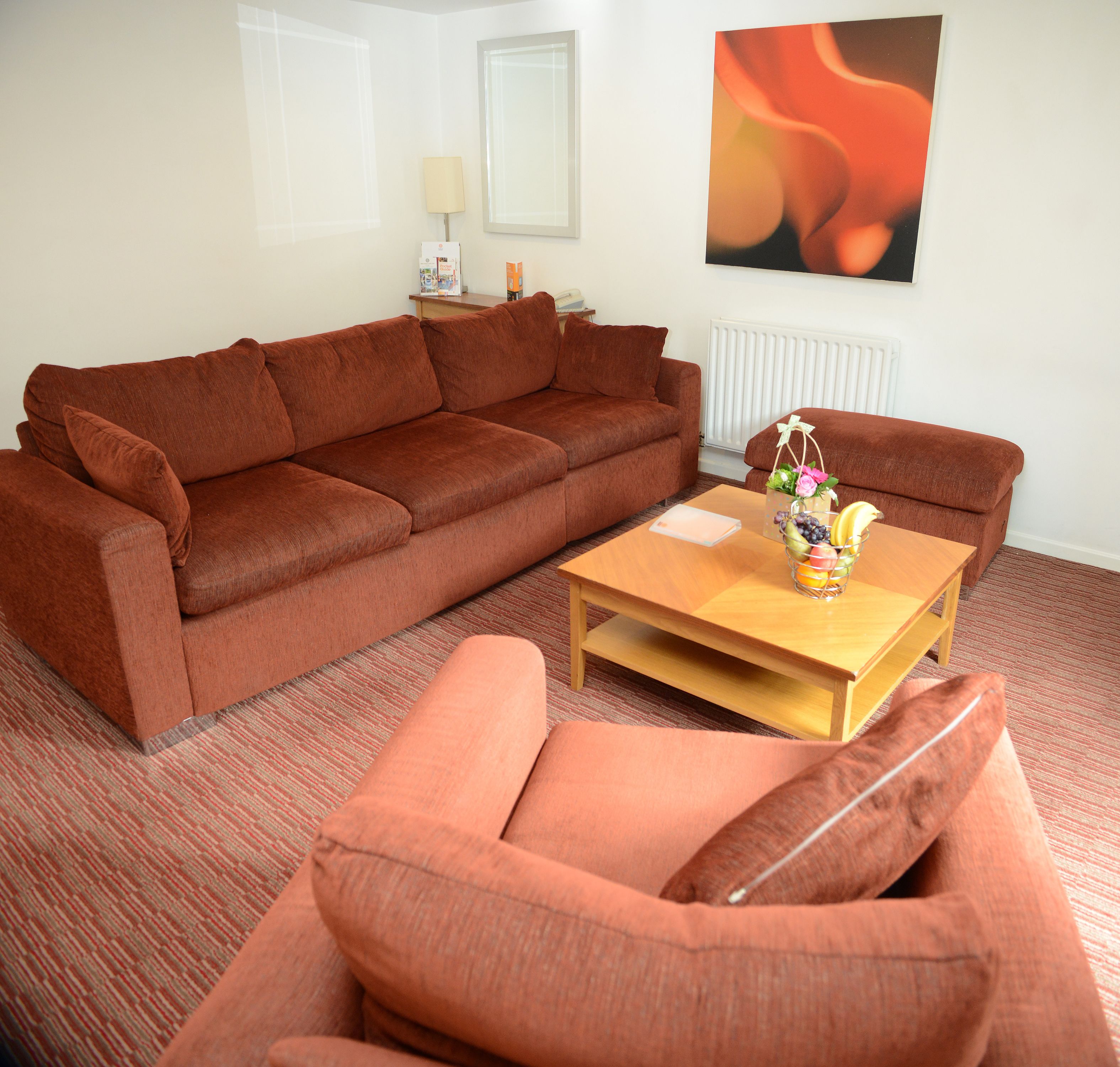 A living room with a brown sofa, a wooden coffee table with a vase of fruit, and a radiator on the wall.